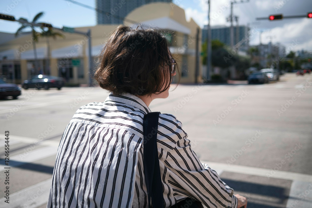 Woman with short hair crosses an urban street on a sunny day, wearing a striped shirt, Miami, Florida, USA Woman with short hair crosses an urban street on a sunny day, wearing a striped shirt, Miami, Florida, USA