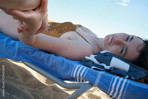 Woman in swimsuit lying on beach chair under clear blue sky, reaching out to person next to her, Miami, Florida, USA photo