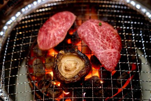 Slices of marbled beef and a mushroom grilling over open flames on a metal barbecue grate. Tokyo, Japan photo