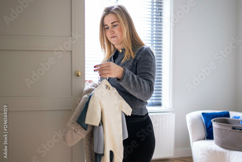 A woman in a gray sweater examines baby clothes while standing in a bright, modern room. Netherlands photo