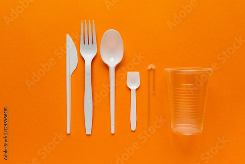 white plastic disposable cutlery on orange bachground (knife, fork, tablespoon, teaspoon, straw, cup)
environmental problem  photo