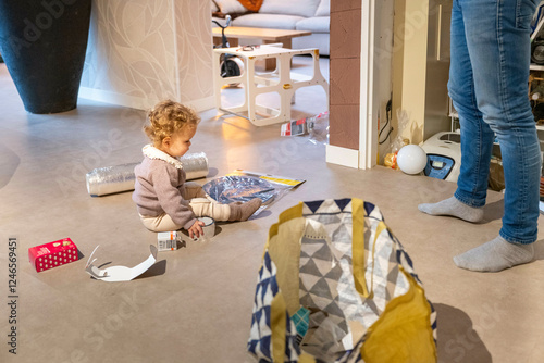 Young child with curly hair plays on the floor surrounded by household items indoors. Netherlands photo