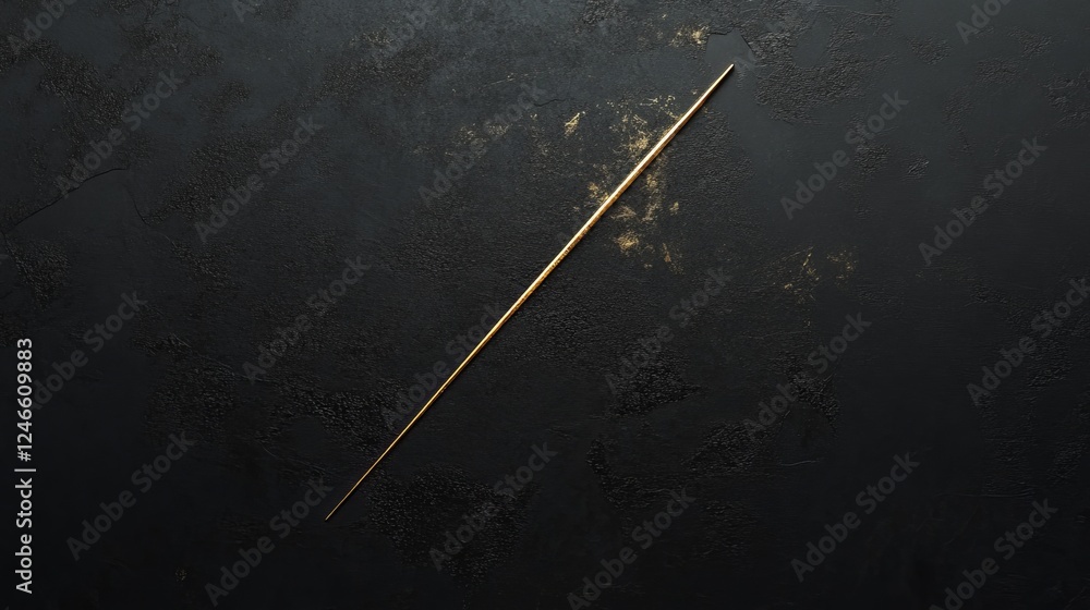 Fototapeta premium Elegant gold stick rests on a textured black surface illuminated by soft light at an artistic angle