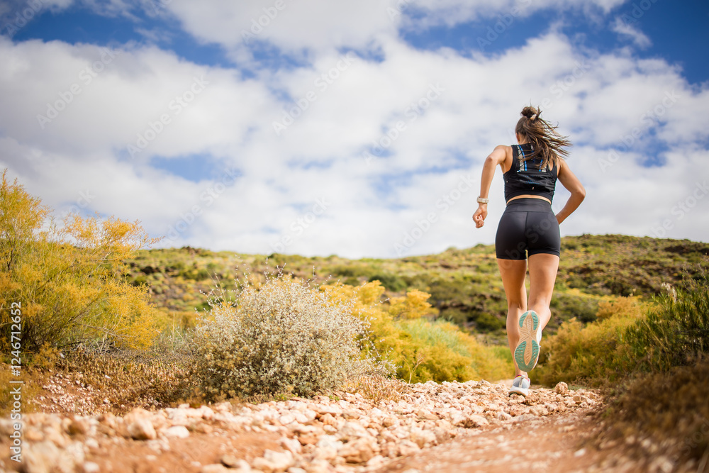 Female trail runner wearing black sportswear and a hydration vest, running through a scenic natural landscape on a rocky path. Female trail runner wearing black sportswear and a hydration vest, running through a scenic natural landscape on a rocky path.