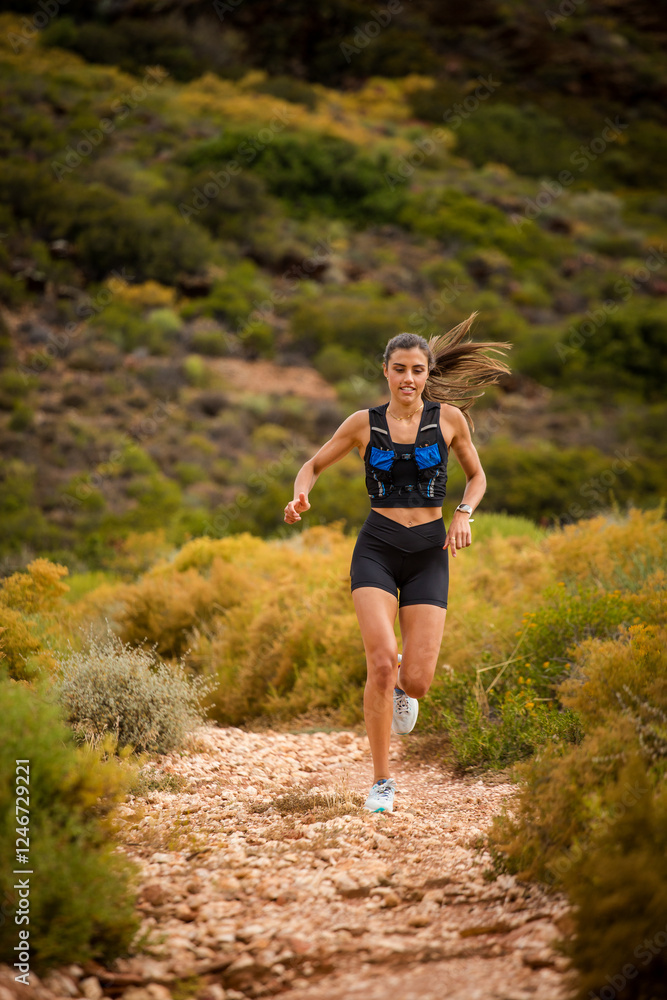 Female trail runner wearing black sportswear and a hydration vest, running through a scenic natural landscape on a rocky path. Female trail runner wearing black sportswear and a hydration vest, running through a scenic natural landscape on a rocky path.