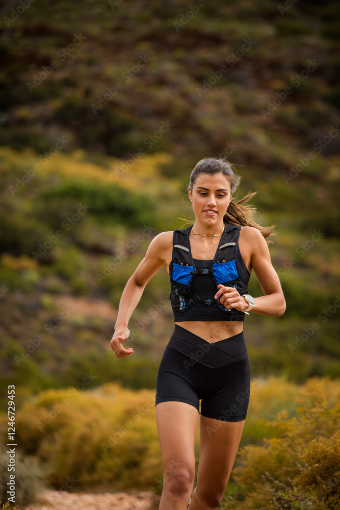 Female trail runner wearing black sportswear and a hydration vest, running through a scenic natural landscape on a rocky path. Female trail runner wearing black sportswear and a hydration vest, running through a scenic natural landscape on a rocky path.