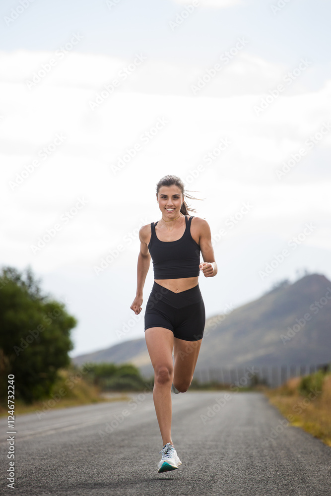 Female athlete in black sportswear running on a rural road with a scenic mountainous backdrop, emphasizing endurance and outdoor fitness. Female athlete in black sportswear running on a rural road with a scenic mountainous backdrop, emphasizing endurance and outdoor fitness.