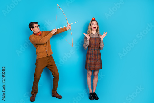 Couple portraying a vintage-inspired humorous scenario of archery with blue backdrop