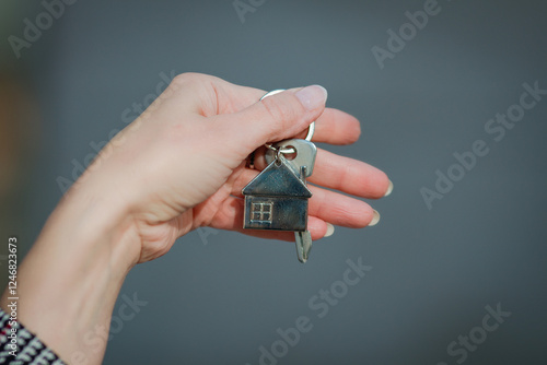 Close-up of a woman's hand holding house keys with a small home-shaped keychain. Symbolizing real estate, new home ownership, or rental property. Minimalistic and elegant composition.