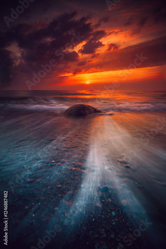 Receding sea washing past a rock on a sandy beach at sunset, Lithuania photo