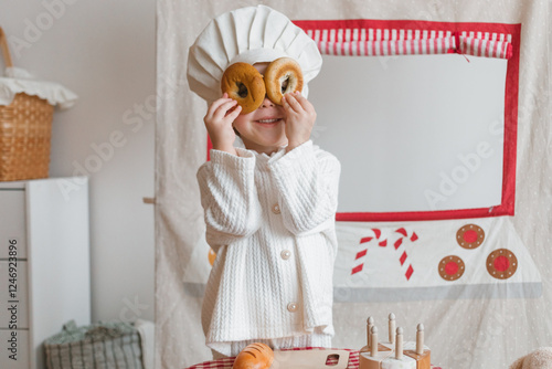 Smiling girl pretending to be a pastry chef covered her eyes with freshly baked bagels