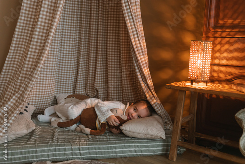 Smiling girl in pyjamas lying on her side in a teepee cuddling a toy monkey photo