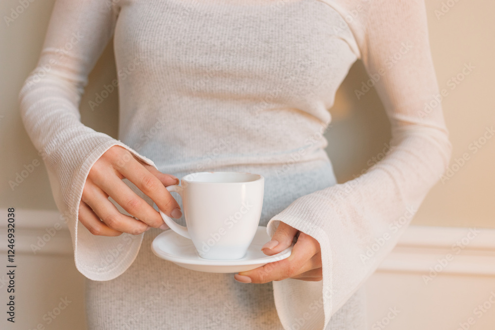 Close-up of an elegant woman in a white dress standing by a wall drinking a cup of coffee Close-up of an elegant woman in a white dress standing by a wall drinking a cup of coffee