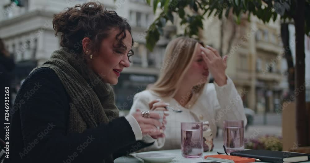 Two friends enjoy coffee and conversation at an outdoor cafe. They are stylishly dressed and engaged in their discussion. Two friends enjoy coffee and conversation at an outdoor cafe. They are stylishly dressed and engaged in their discussion.