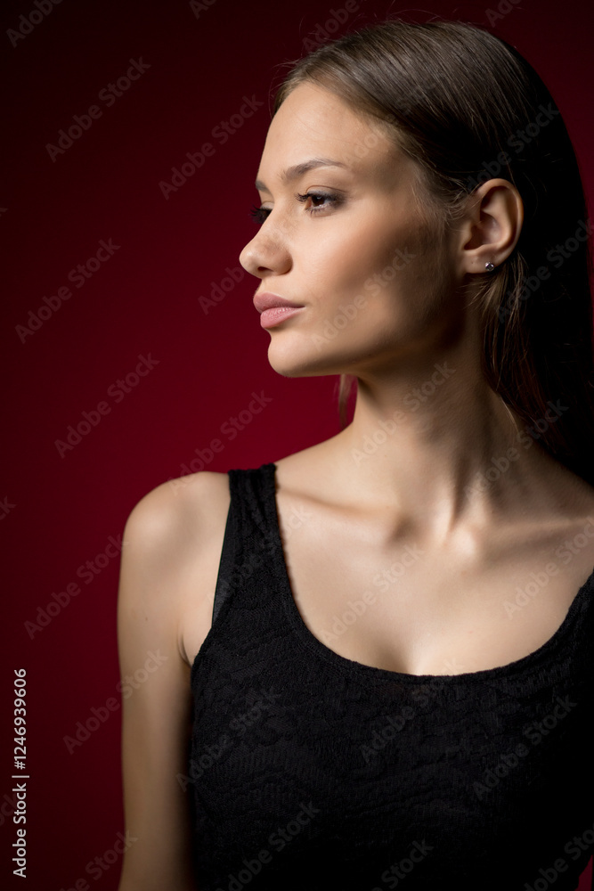 Fototapeta premium Dramatic profile portrait with burgundy background. Elegant side view emphasizes model's features while chiaroscuro lighting creates sophisticated mood