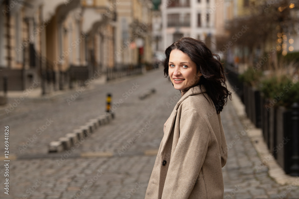 Fototapeta premium A woman walks down a charming cobblestone street, smiling as she enjoys the vibrant atmosphere of the urban environment. The buildings and midday light create a warm ambiance