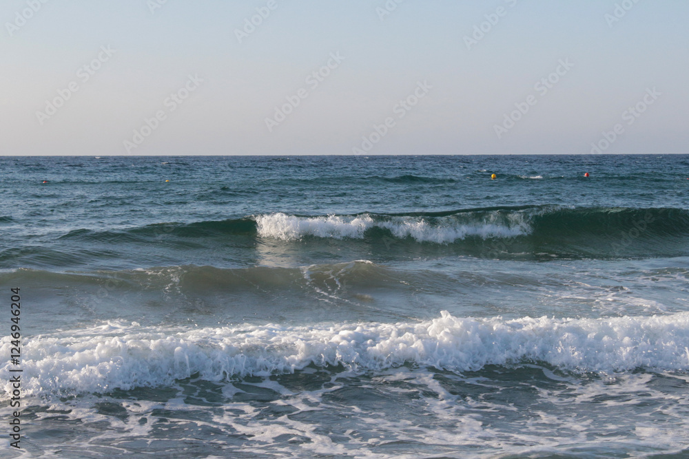 Fototapeta premium Beach of luxury hotel. sunny day, windy, stormy, wavy sea, blue sky. On the beach shines soft yellow-gold brown-golden sand. Sea waves crashing on the shore with wavy white foam. on island of cyprus 