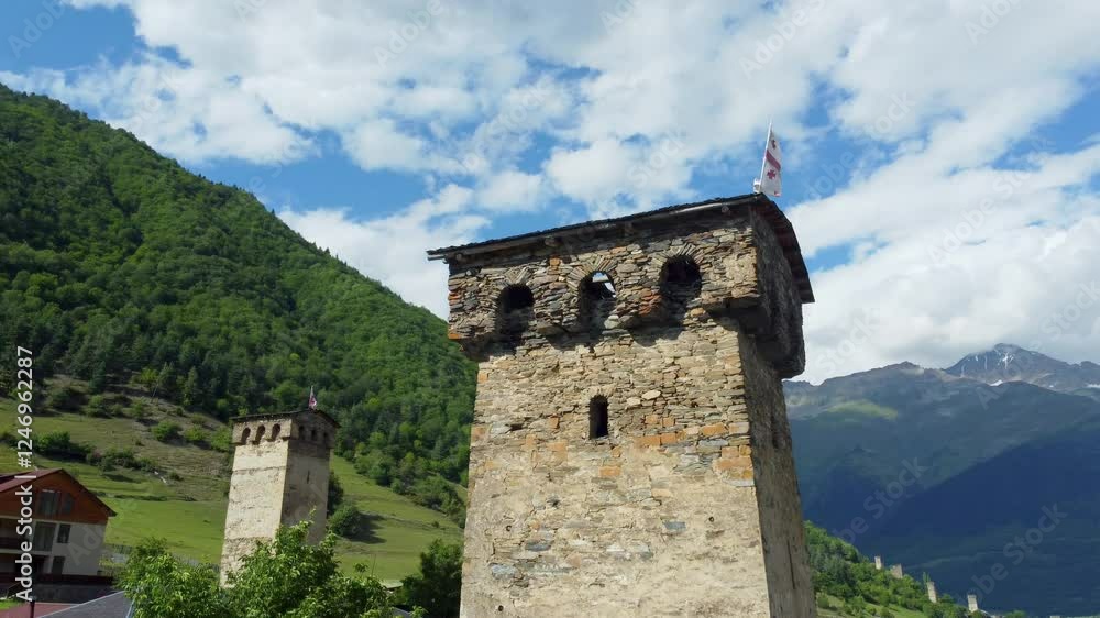 Majestic Svan towers rise against backdrop of green mountains, proudly displaying Georgian flag, symbol of rich history and cultural heritage of region Drone Footage. Majestic Svan towers rise against backdrop of green mountains, proudly displaying Georgian flag, symbol of rich history and cultural heritage of region Drone Footage.