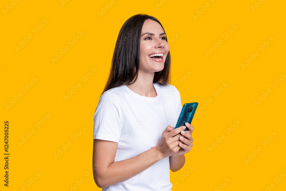 Naklejka premium Millennial laughing woman blogging on phone or using communication chat on smartphone isolated on yellow