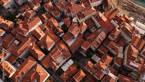Top view of an old European town with terracotta roofs creating an atmospheric pattern. The composition shows a dense urban layout with winding streets, tiled roofs and historical architecture.