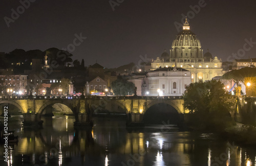 A night view of St. Peter's Basilica in the Vatican seen from across the Tiber River. The Ponte Sant'Angelo bridge is visible in the foreground, with its arches and reflections.