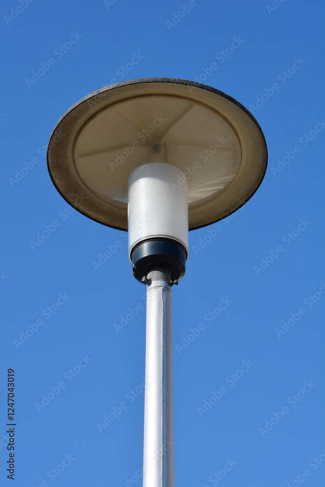 A low-angle shot of a modern street lamp with a round, flat, gray luminaire against a clear blue sky A low-angle shot of a modern street lamp with a round, flat, gray luminaire against a clear blue sky