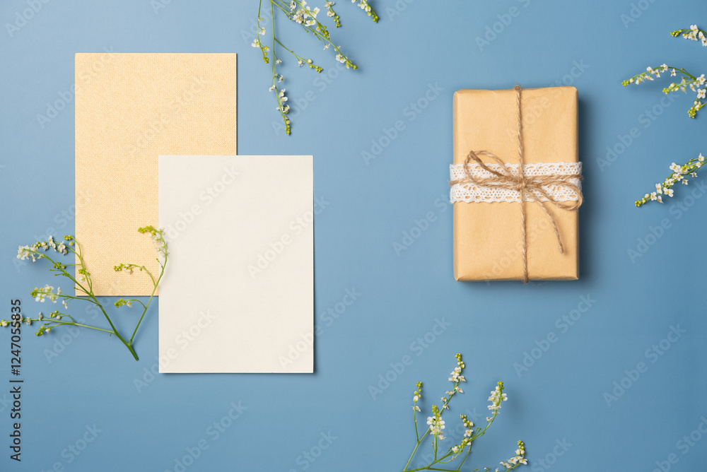 Paper blank sheet with bouquet of flowers and gift box on blue background. Flat lay, top view. Paper blank sheet with bouquet of flowers and gift box on blue background. Flat lay, top view.