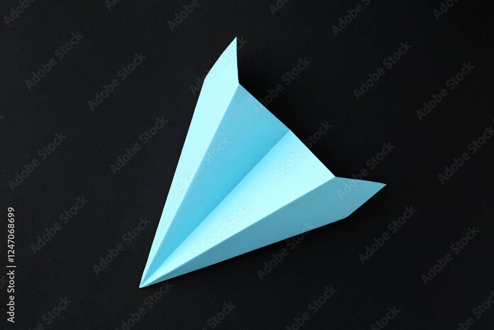 Fototapeta premium One handmade light blue paper plane on black background, top view