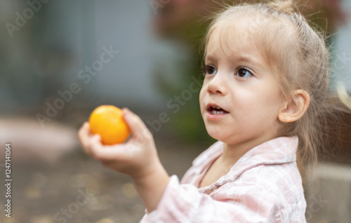 A young girl holds up a small orange fruit and looks with indignation. photo