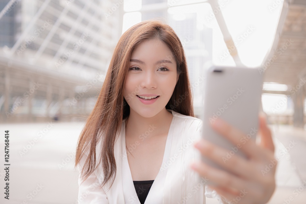 A young woman smiling while taking a selfie in an urban setting.