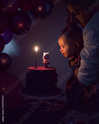 Obraz na płótnie Dad holds his daughter in a dress and a hat for 1 year in front of the cake and blows out the candle. w salonie
