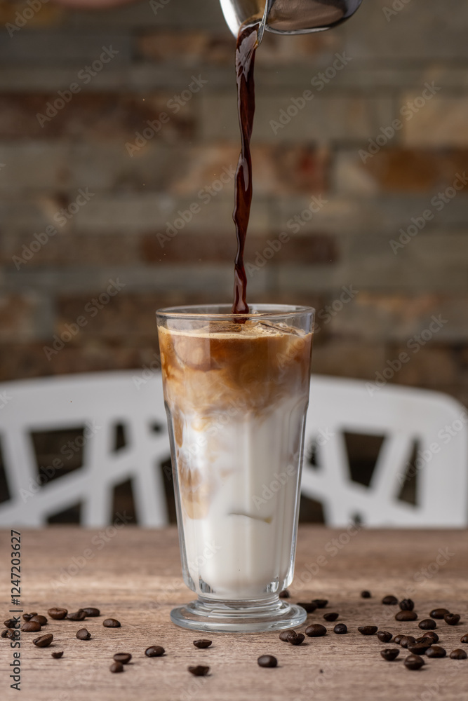 Making iced latte in a tall glass with ice by adding coffee to milk
