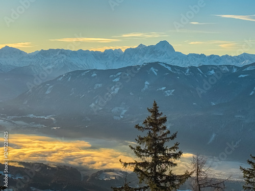 Scenic view from Bad Bleiberg, Carinthia, Austria. Fog covered alpine valley surrounded by majestic snow capped mountain peaks of Julian Alps. Winter hiking in wild remote Austrian Alps at sunrise photo