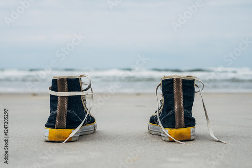 Close-up rear view of a pair of sneakers on a sandy beach by water's edge photo