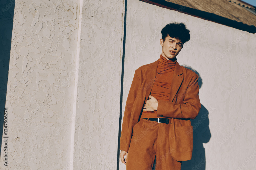 Fototapeta premium Stylish young man in an orange suit against a textured white wall, exuding confidence and contemporary fashion