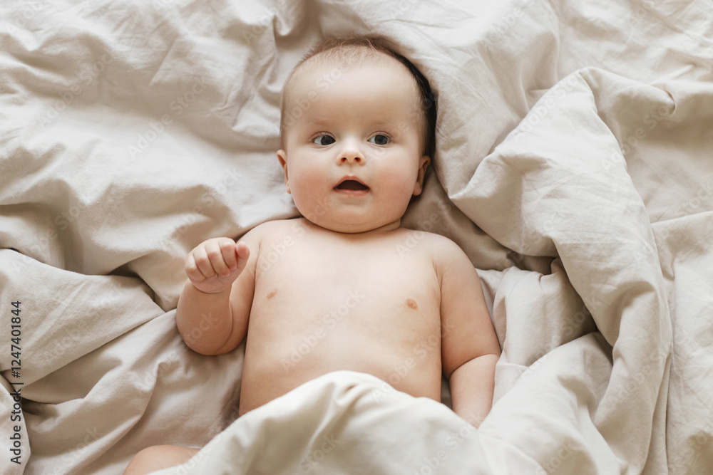 Cute little baby lying in beige bed sheets in morning light. Bedtime. Happy adorable infant portrait after sleep, top view with space for text. Childhood and childcare Cute little baby lying in beige bed sheets in morning light. Bedtime. Happy adorable infant portrait after sleep, top view with space for text. Childhood and childcare