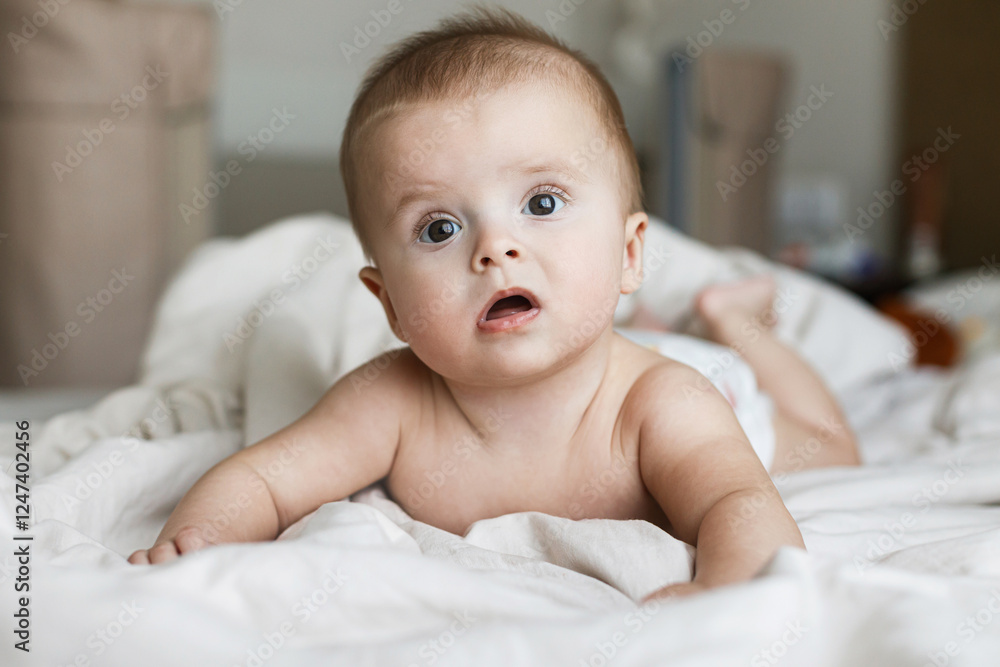 Cute little baby lying in beige bed sheets. Bedtime or morning wake up. Happy adorable infant portrait with funny emotion, space for text. Childhood and childcare
