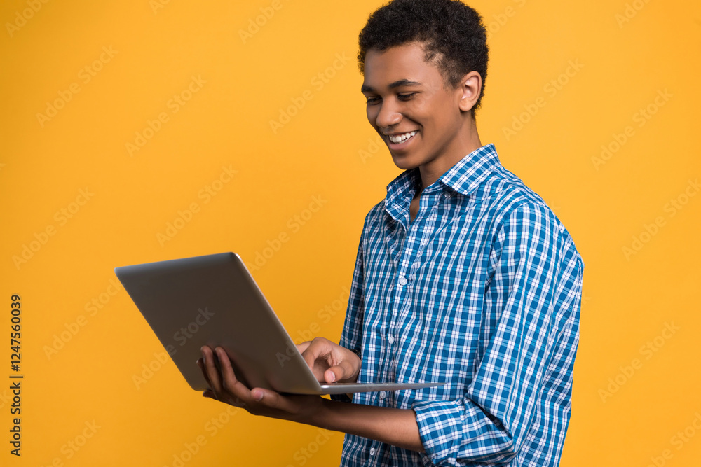 Afro American teenager working with laptop. Isolated on yellow background. Studio portrait. Afro American teenager working with laptop. Isolated on yellow background. Studio portrait.