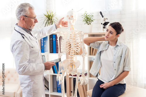 Doctor in white gown with stethoscope and female patient in office. Patient's neck hurts.
