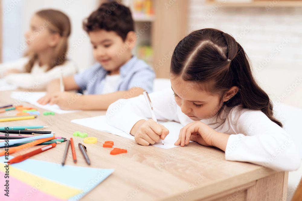 Children write in notebooks with a pen. They are sitting at the table. They are helped by an adult teacher. Children together Children write in notebooks with a pen. They are sitting at the table. They are helped by an adult teacher. Children together