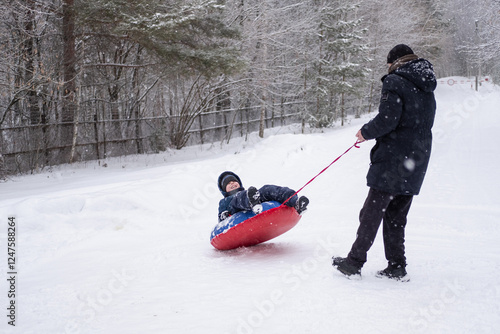 a child flips over from snow tubing while riding with his dad against the backdrop of a winter forest. Dangerous skiing in winter. Children's injuries during winter sports