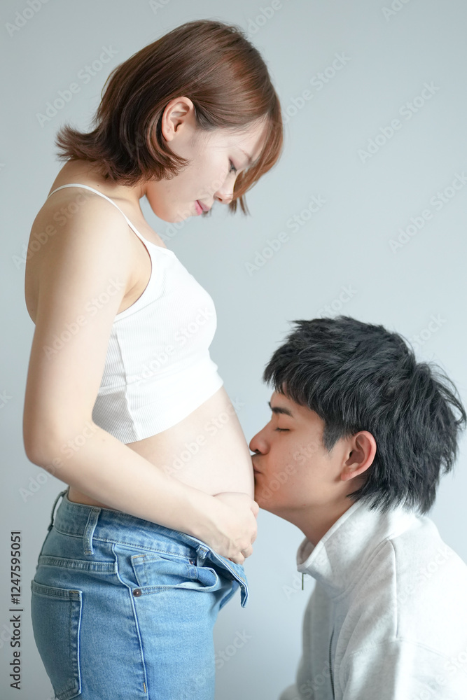 A Japanese pregnant woman in her 20s dressed to show her stomach and her husband kissing her stomach in an apartment room A Japanese pregnant woman in her 20s dressed to show her stomach and her husband kissing her stomach in an apartment room