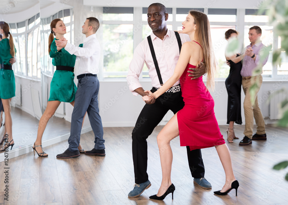 Fototapeta premium With unhurried music, woman with African man in couple spins to rhythm of waltz during lesson for novice students. Classes in mini-groups for those who want to learn dancing