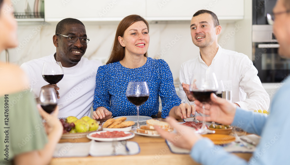 Multiethnic women and men friends talking and drinking wine in the kitchen Multiethnic women and men friends talking and drinking wine in the kitchen