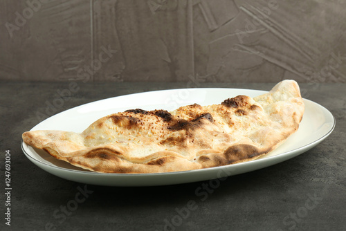 One delicious calzone on grey textured table, closeup photo