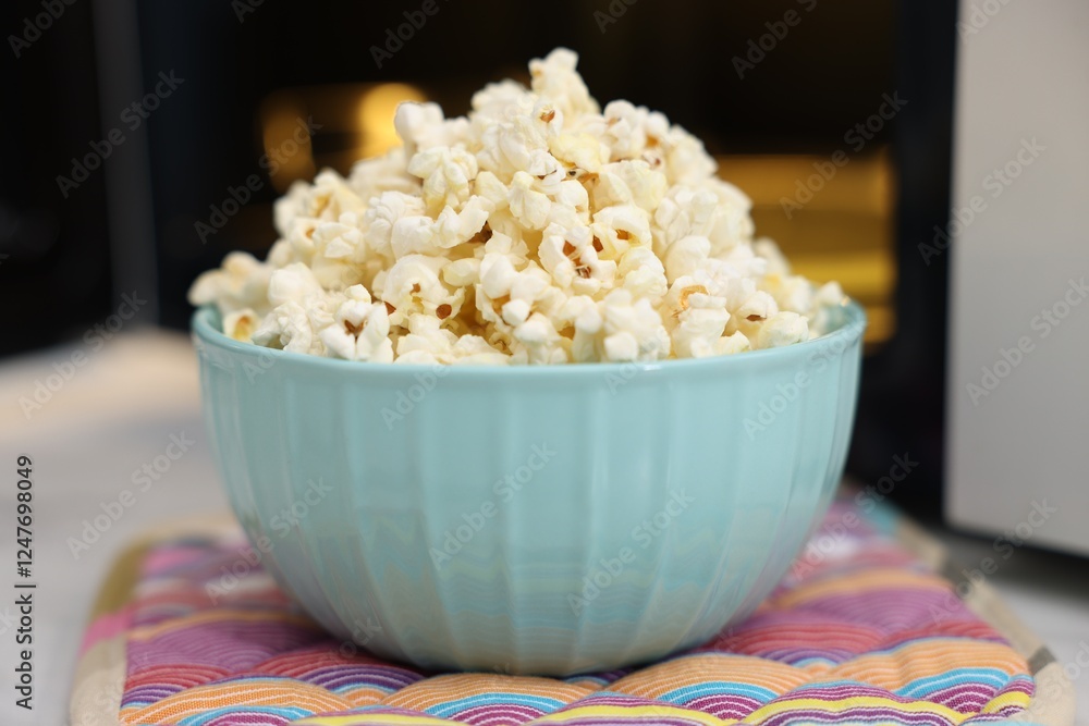 Tasty popcorn in bowl near microwave oven on table, closeup Tasty popcorn in bowl near microwave oven on table, closeup