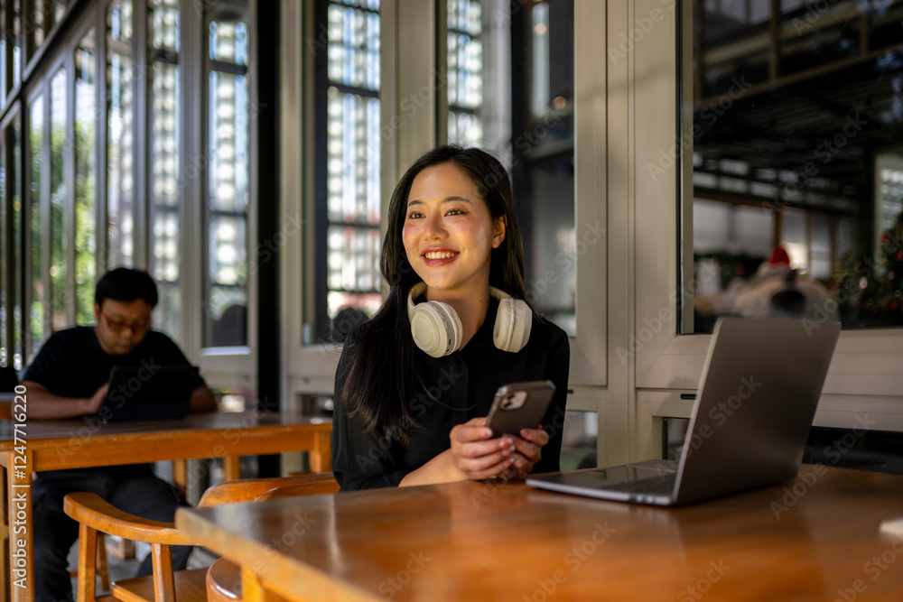 A woman is sitting at a table with a laptop and a cell phone A woman is sitting at a table with a laptop and a cell phone