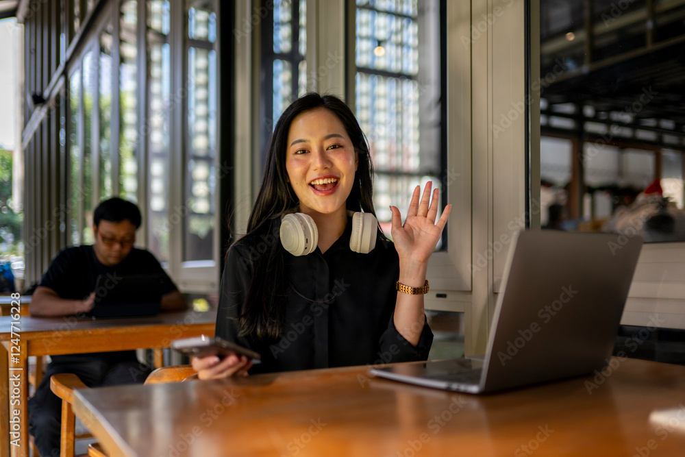 © Wasana - A woman wearing headphones is smiling and waving at the camera