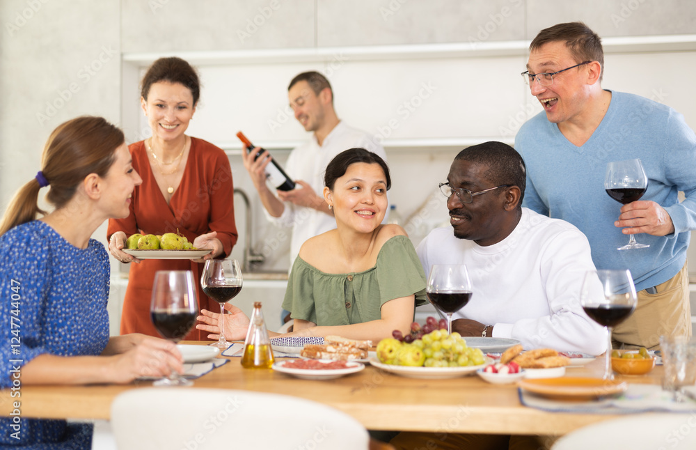 Happy adult friends at the festive table discussing the news and drinking red wine Happy adult friends at the festive table discussing the news and drinking red wine
