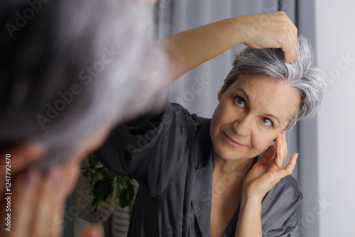An adult well-groomed woman of age during menopause with gray hair examines the amount of gray hair